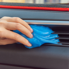Hand using blue multipurpose car cleaning gel to remove dust from air vent.